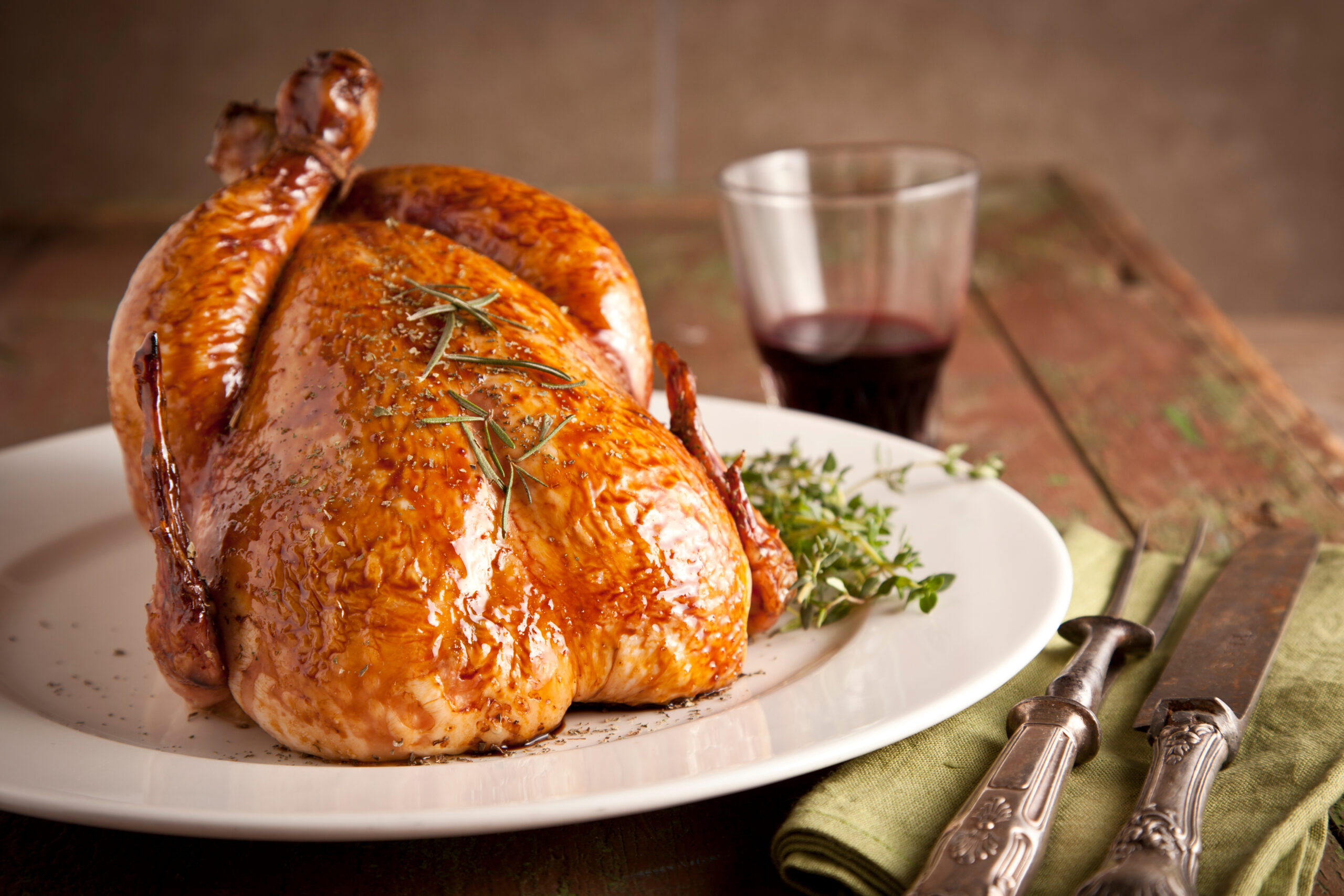 Roasted whole chicken garnished with fresh thyme and served with lemon wedges on a black slate board, with kitchen knives in the background.