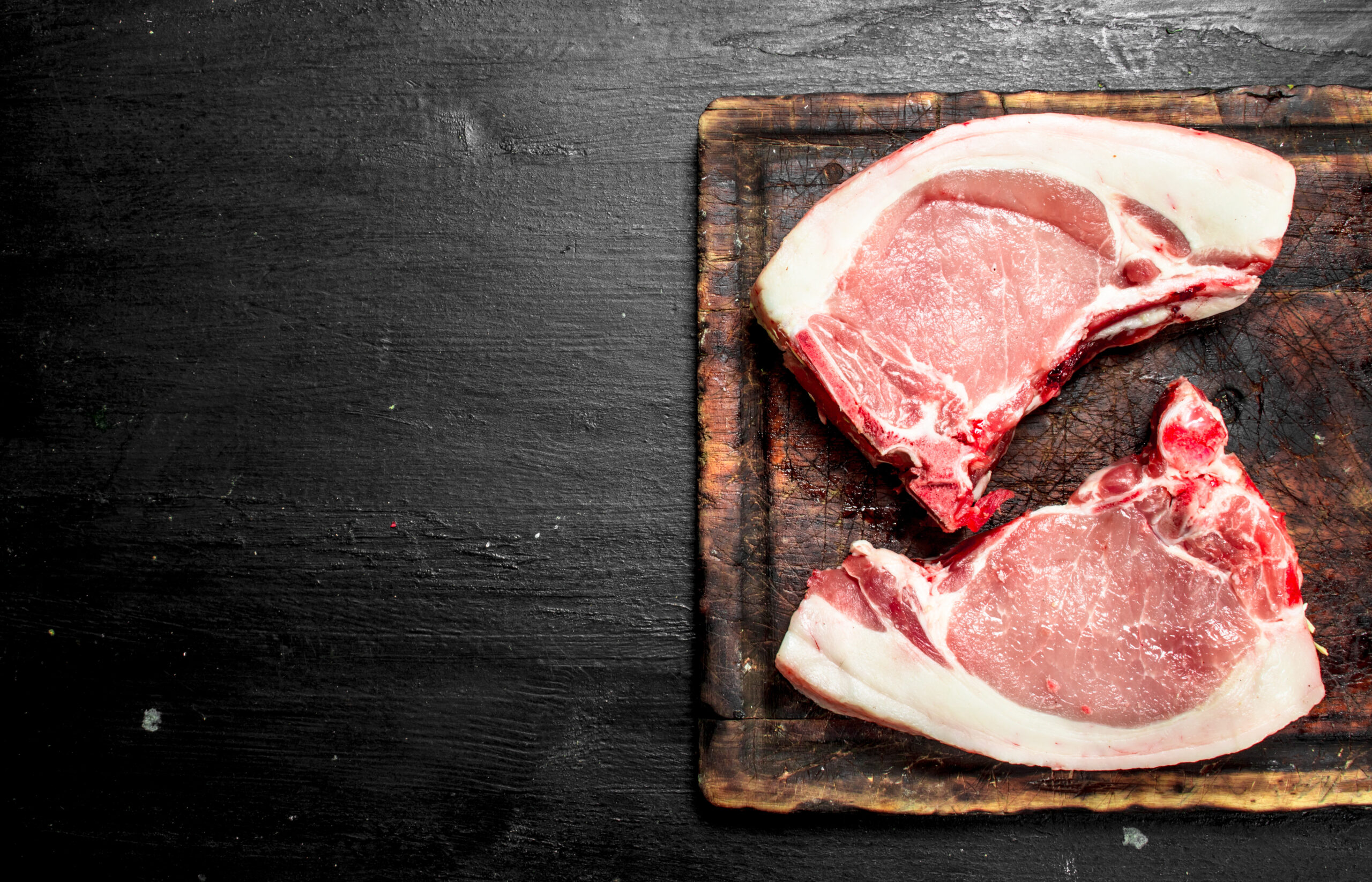 Succulent pulled pork on a wooden cutting board, showcasing tender, shredded meat with a crispy outer layer. A fork rests beside the meat, highlighting its juicy texture and rich seasoning.